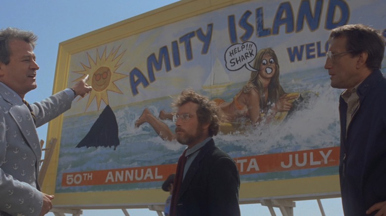 Murray Hamilton as Mayor Larry Vaughn, Richard Dreyfuss as Hooper, and Roy Scheider as Chief Brody, pointing at an Amity Island billboard that's been graffiti'd to show a woman swimming away from a shark