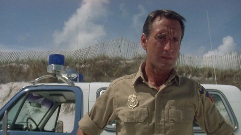 Roy Scheider as Chief Brody in Jaws, standing in front of his truck on the beach looking concerned