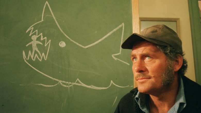 Quint sits in front of chalkboard drawing of shark