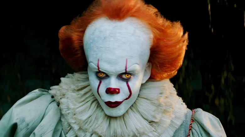 Bill Skarsgard portrays Pennywise the Clown, frocked in white and crowned with ginger hair, in It