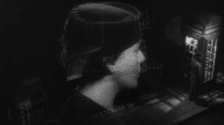 Double-exposed shot of Lucie Mannheim as Miss Smith speaking in profile and a man standing by a telephone booth in The 39 Steps