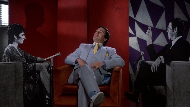 Robert De Niro as Rupert Pupkin sitting between black-and-white cutouts of Liza Minnelli and Jerry Lewis as Jerry Langford