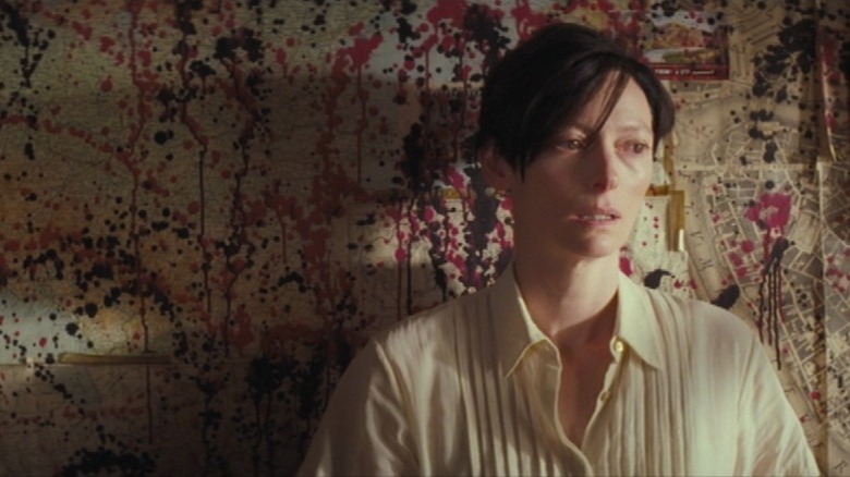 Tilda Swinton as Eva Khatchadourian leaning against a wall covered in maps and paint splatters in We Need to Talk About Kevin