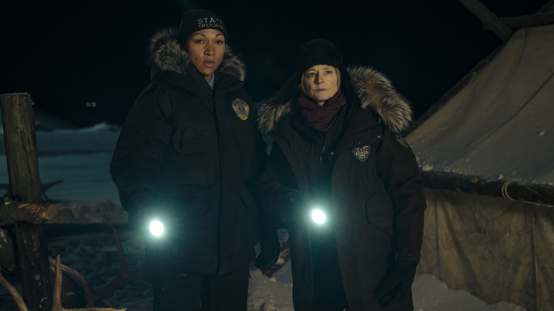 Kali Reis' Evangeline and Jodie Fosters' Liz, dressed for snow, shine flashlights in the dark in True Detective: Night Country