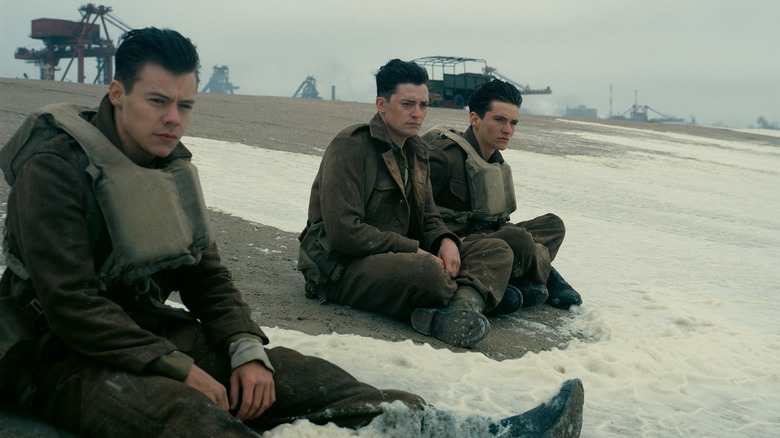 Alex (Harry Styles), Gibson (Aneurin Barnard), and Tommy (Fionn Whitehead) sitting on the beach in Dunkirk