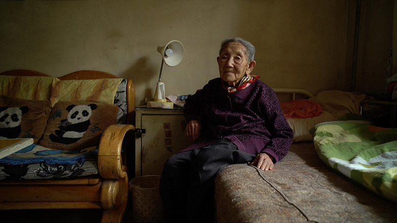 Gao Guifang sits on her bed next to a couch in "Dead Souls"