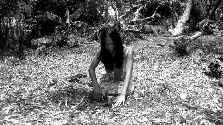 A Filipino woman digs a hole in the dirt with her hands in "Death in the Land of Encantos"