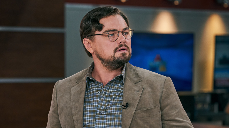 Leonardo DiCaprio as Dr. Randall Mindy in Don't Look up, sitting at a desk with glasses on, looking perplexed