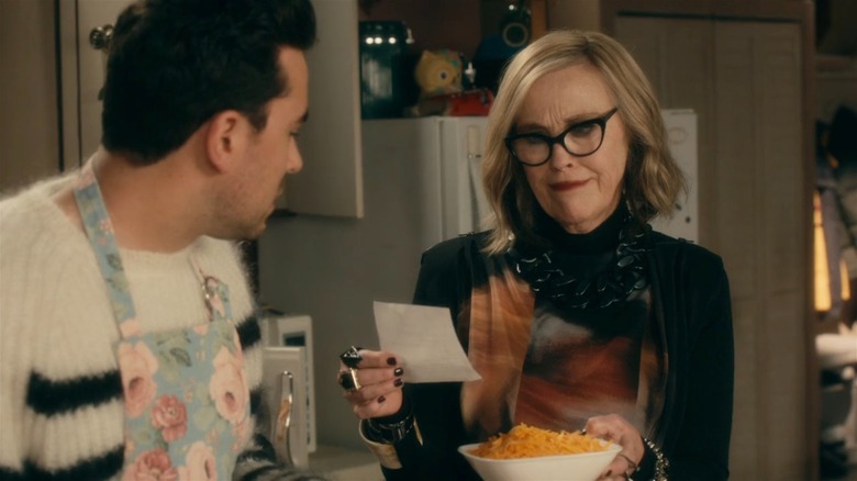 Moira and David stand in a kitchen, and Moira holds up a recipe card