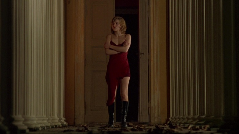 Milla Jovovich as Alice, walking through an abandoned mansion in a red night dress in the 2002 Resident Evil film