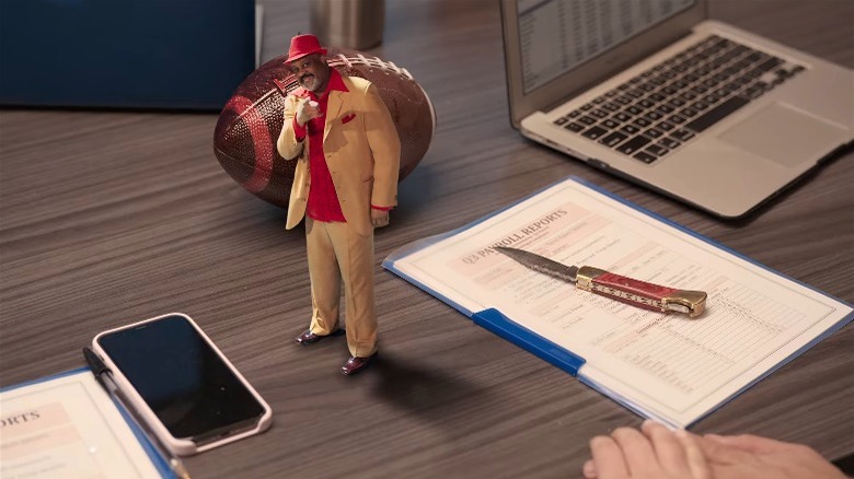 a desk featuring a phone, a tiny pimp, a knife, and a laptop