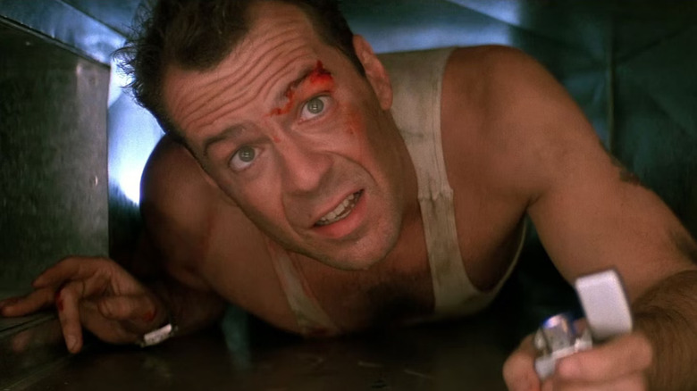 Bruce Willis as John McClane crawling through an air vent with a lighter in his hand in Die Hard.