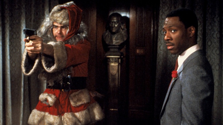 Dan Aykroyd as Louis Winthorpe III dressed as Santa Claus pointing a gun and Eddie Murphy as Billy Ray Valentine staring in the gun's direction in Trading Places.