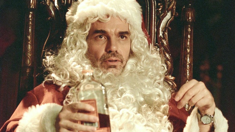 Billy Bob Thornton as Willie T. Stokes sitting on a wooden chair wearing a Santa outfit and holding a bottle of alcohol in Bad Santa.