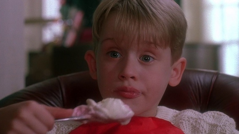 Macaulay Culkin as Kevin McCallister sitting in a chair eating ice cream in Home Alone.