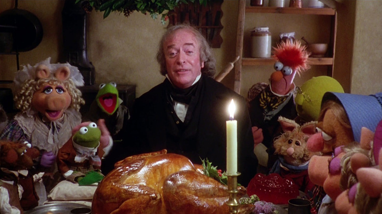 Michael Caine as Ebenezer Scrooge sitting at the dinner table with a big turkey and the Muppets surrounding him in The Muppet Christmas Carol.