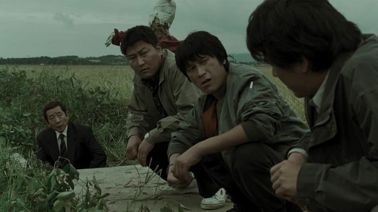 A group of detectives investigate a crime scene in Memories of Murder.