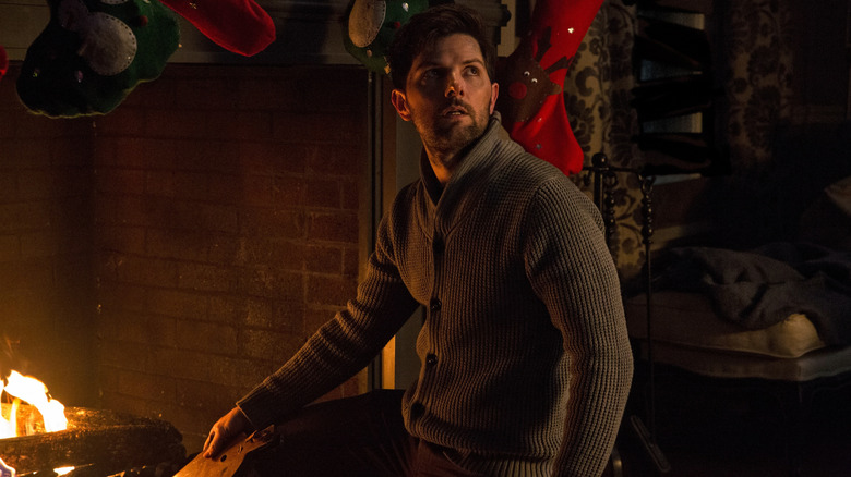 Tom, played by Adam Scott, poking at a Christmas fireplace, looking over his shoulder in Krampus.