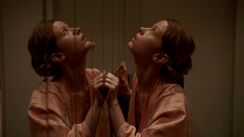 Sara Simms, standing up against a mirrored wall, looking worried at the ceiling in Suspiria