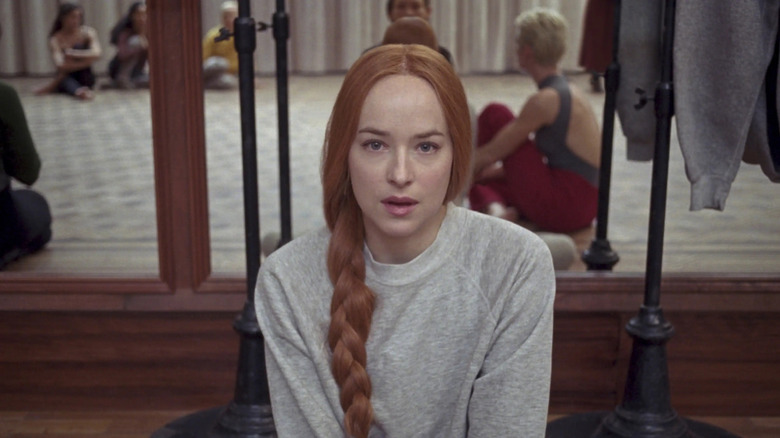 Susie Bannion, sitting on the floor of a dance studio. Other dancers are seen seated in the mirror behind her in Suspiria