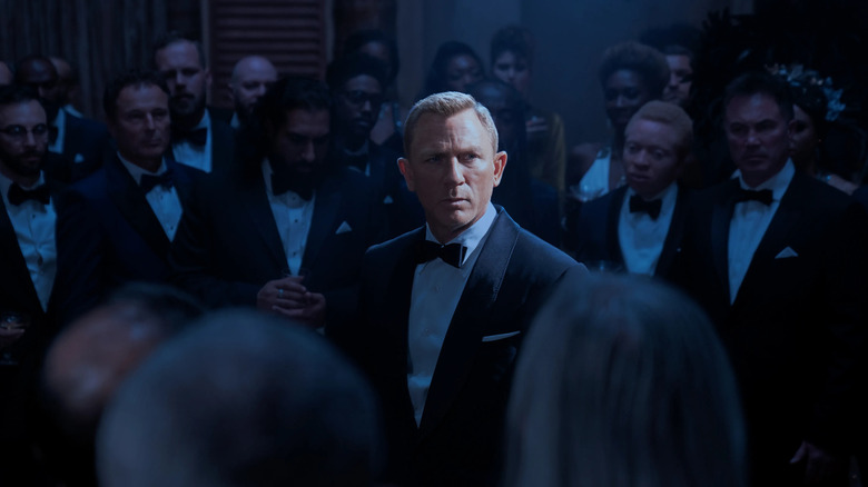 James Bond surrounded by people in tuxedos in No Time to Die