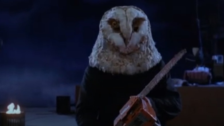 Person in an owl mask holding a chainsaw