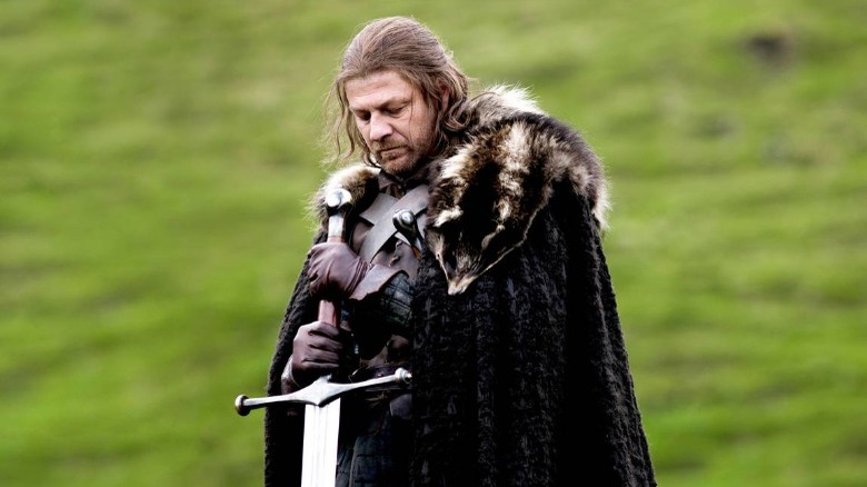 Ned Stark holding sword on grassy hill