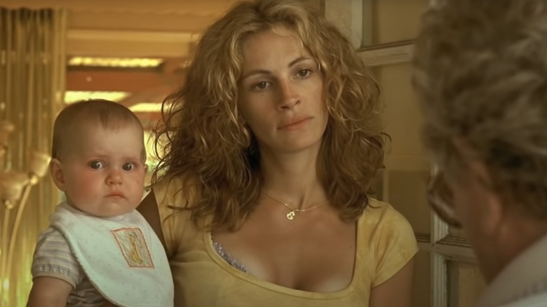 Julia Roberts as Erin Brockovich talks to a man while holding a baby.