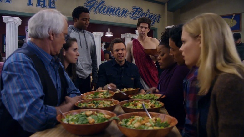 Community's Jeff speaking in front of various salad plates while Pierce, Annie, Troy, Dean Pelton, Shirley, Abed, and Britta listen