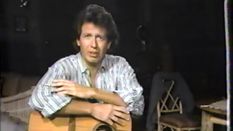 It's Garry Shandling's Show's Garry Shandling addressing the camera while leaning on a guitar