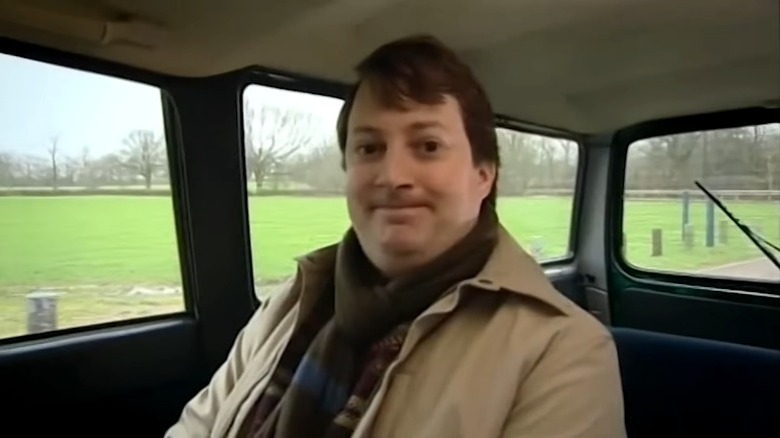 Peep Show's Mark grinning awkwardly in the back of a car and looking at the camera