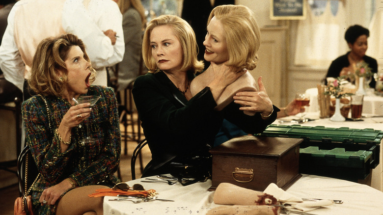 Maryann and Cybill shocked at a table as Cybill holds a model of her own head