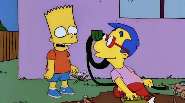 Bart stands next to Milhouse as he plays in the mud outside in The Simpsons