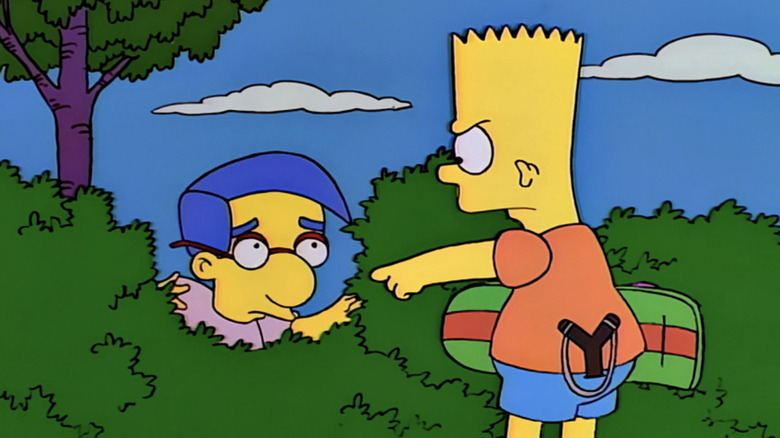 Bart points angrily at Milhouse, who cowers in the bushes in The Simpsons