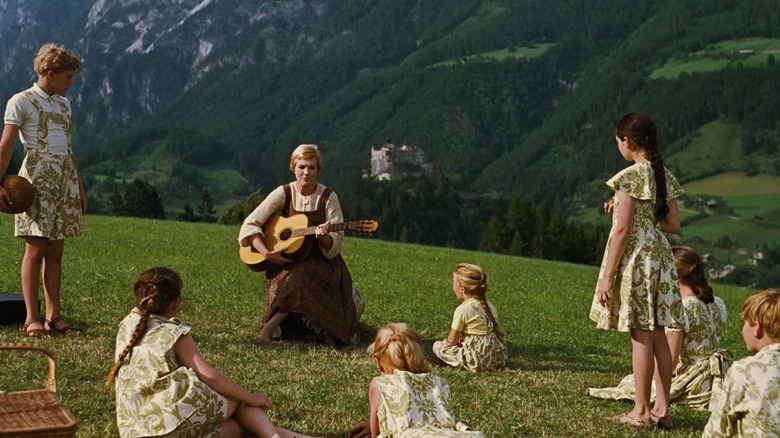 Maria sitting with a guitar in the Alps, the Von Trapp children gathered around her