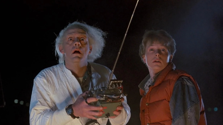 Michael J. Fox and Christopher Lloyd as Marty McFly and Doc Brown standing in a parking lot in Back to the Future