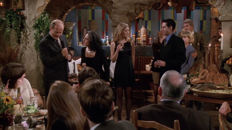 Frasier stands in a restaurant being berated by his Greek aunt as his family and dinner guests look on