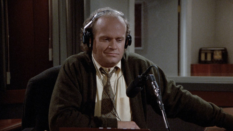 Frasier sits with headphones on at his desk in the radio studio