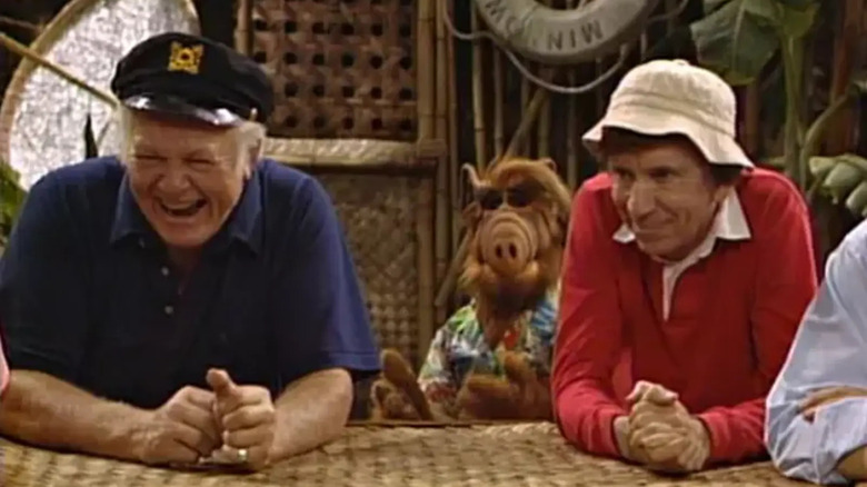 O capitão e Gilligan em uma mesa, com Alf atrás deles