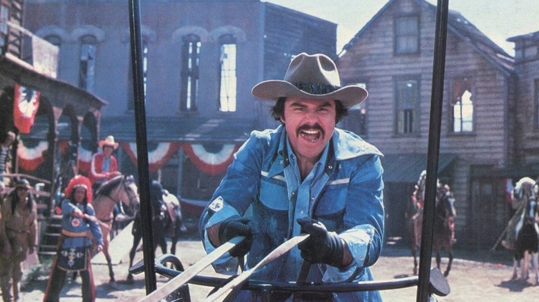 Burt Reynolds leading a chariot race through a Wild West set