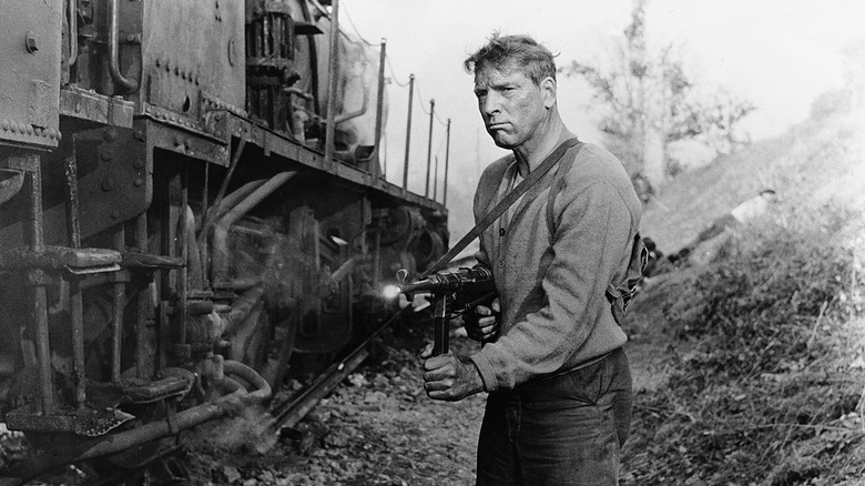 Burt Lancaster firing an MP40 machine gun beside a train