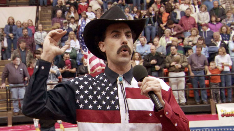 Borat in an American flag button down shirt and cowboy hat at a rodeo