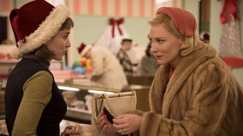 Rooney Mara as Therese Belivet in a Santa hat across a department store counter from Cate Blanchett's Carol Aird wearing a fur coat in Carol