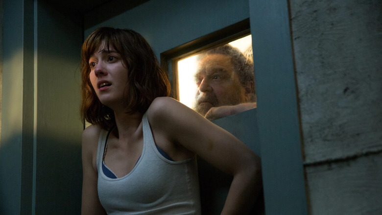 Michelle looks frightened while Howard Stambler watches from the other side of a door in 10 Cloverfield Lane