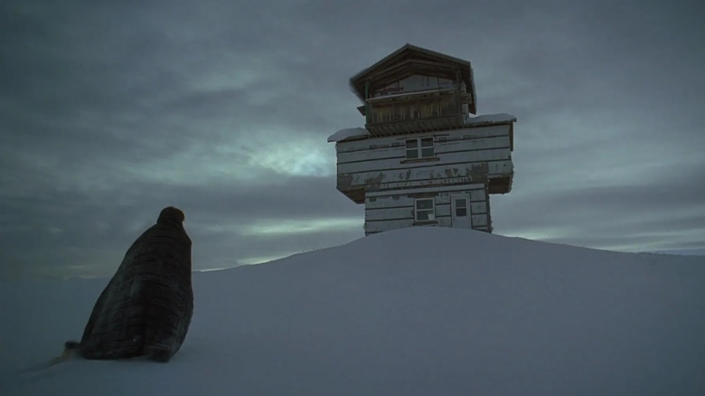 Grace stands in the snow and looks at a strange building in The Lodge