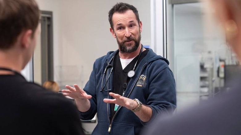 Noah Wyle's Dr. Robby explains something to two people who are facing away from camera in The Pitt