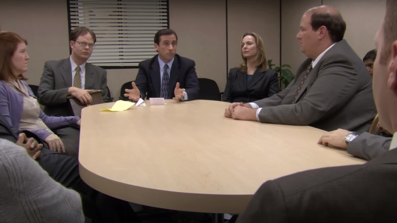 Kate Flannery's Meredith, Rainn Wilson's Dwight, Steve Carrell's Michael, Melora Hardin's Jan, Brian Baumgartner's Kevin sit around a conference table in The Office