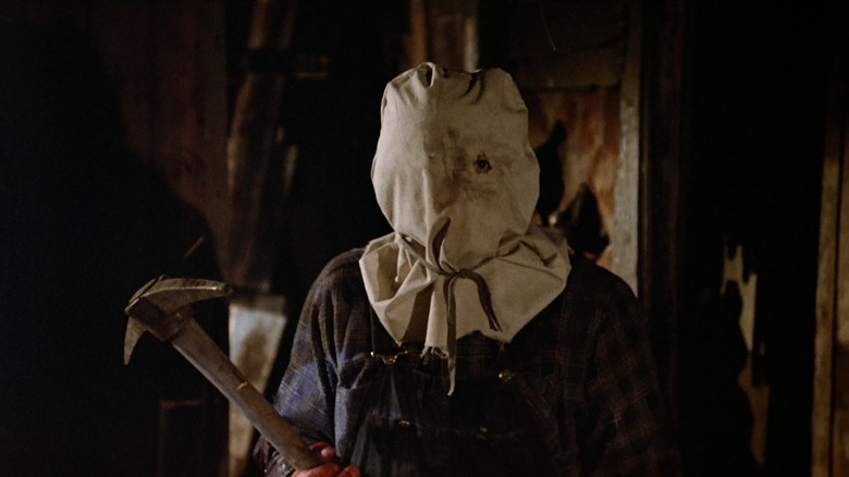 A figure wearing a burlap sack over their head carrying a pick axe