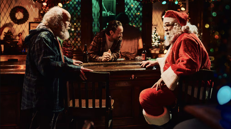 A bearded Clint Howard as Smokey and Daniel Roebuck as Charlie in a Santa Claus suit laughing in Terrifier 3