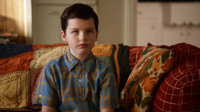 Young Sheldon sitting on a couch, looking at someone off camera in Young Sheldon